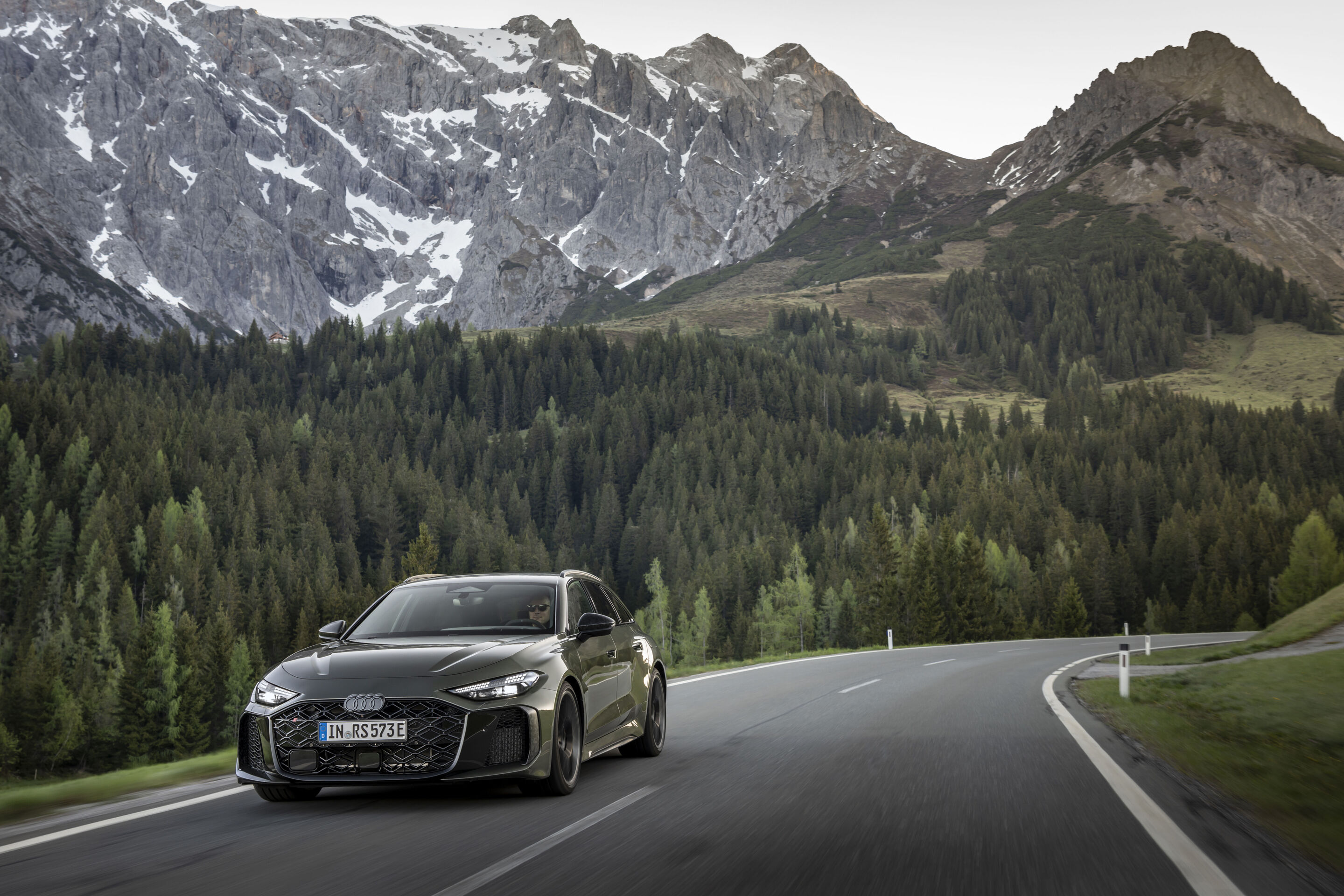 Audi RS 5 Avant - Audi RS 5 Avant in Bedford green, outdoor driving shot, exterior, three-quarter front view on a winding road in front of an alpine mountain backdrop.