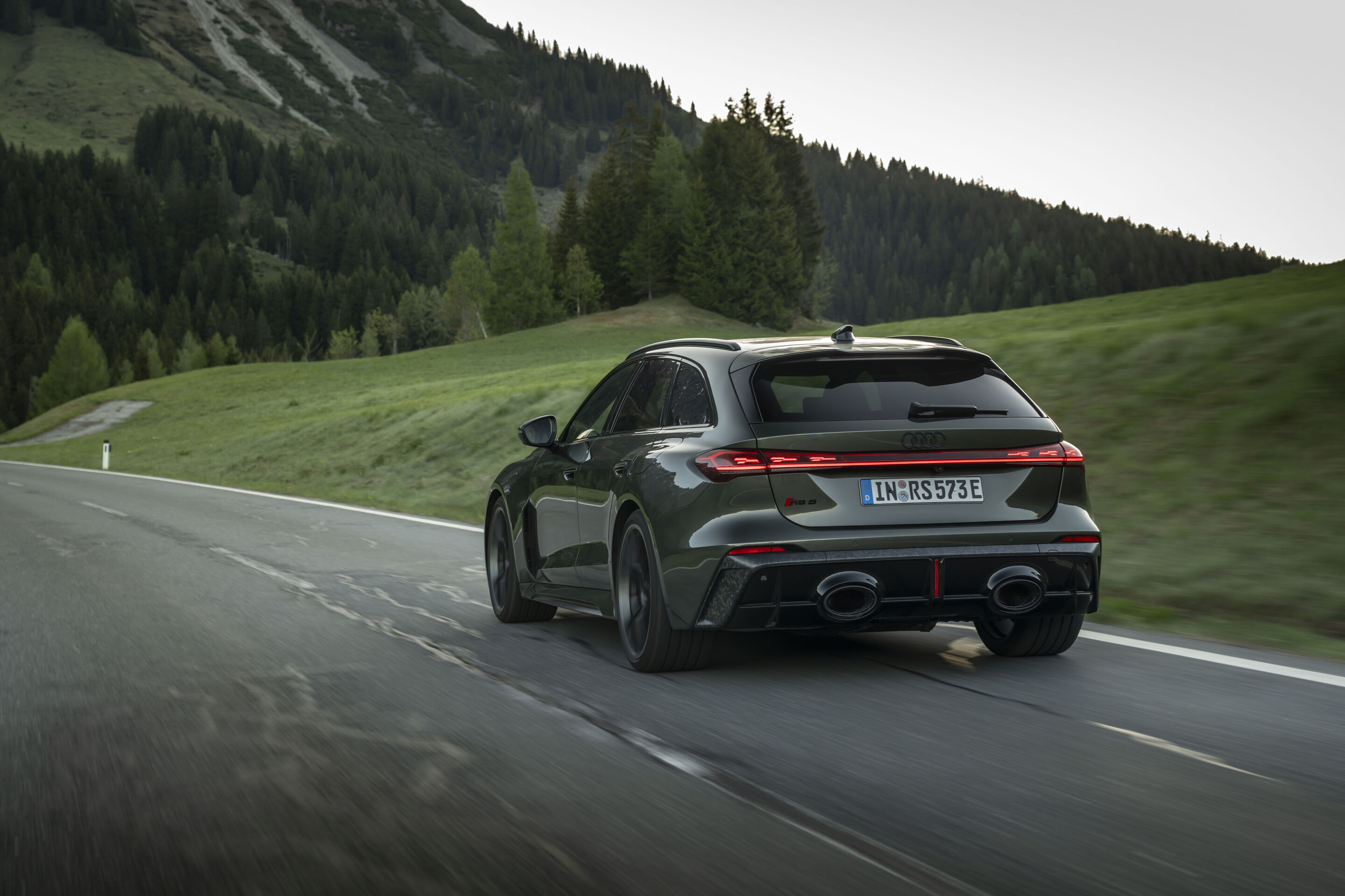 Audi RS 5 Avant - Audi RS 5 Avant in Bedford green, outdoor driving shot, exterior, rear view on a winding country road in a mountainous landscape.