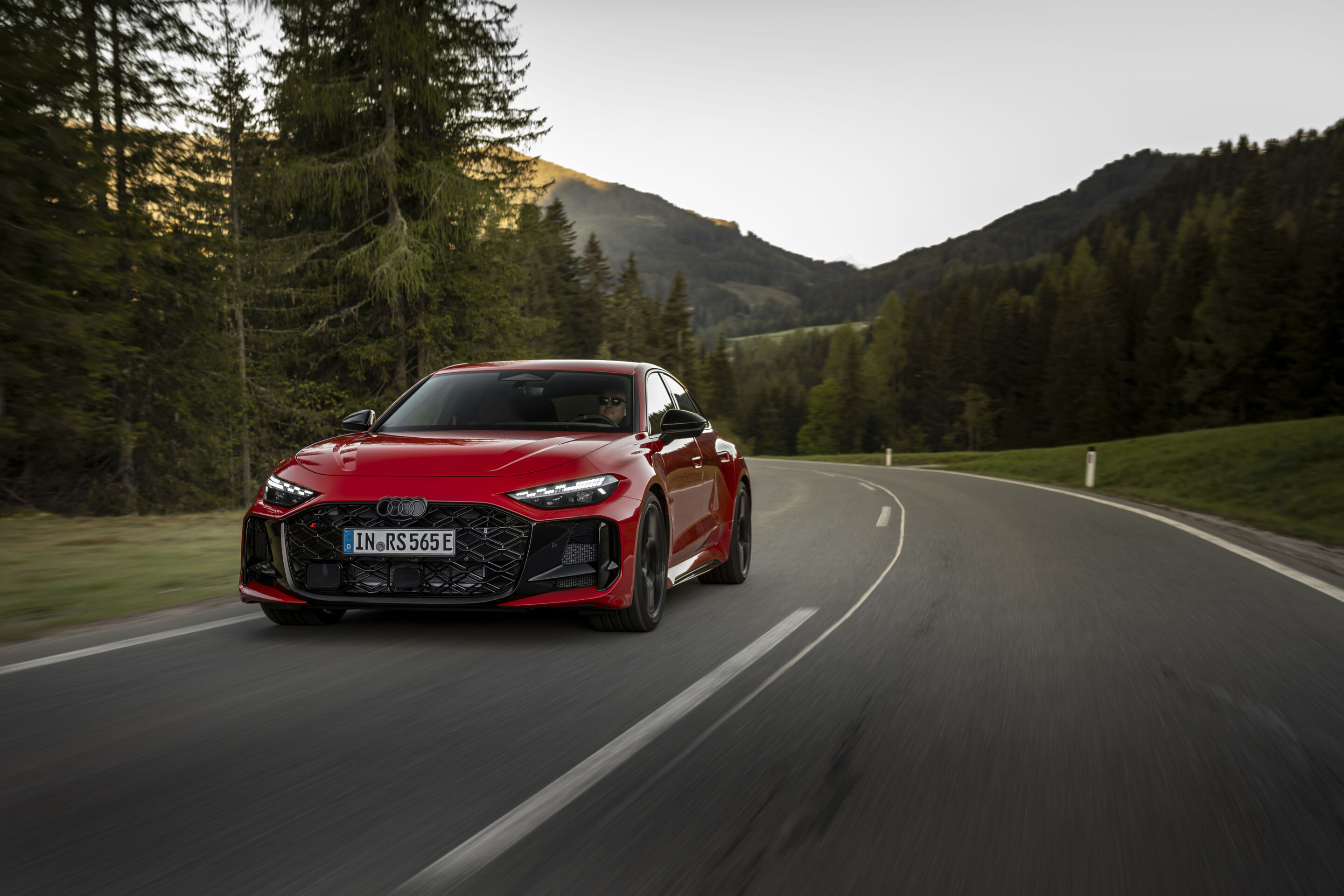 Audi RS 5 Sedan - Audi RS 5 Sedan in Progressive red, outdoor driving shot, exterior, three-quarter front view on a winding country road.