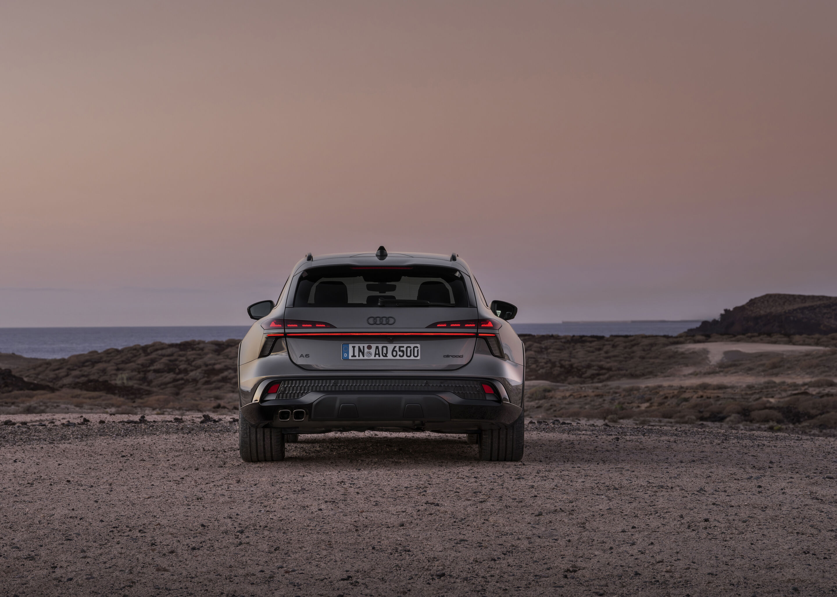 Audi A6 allroad quattro - Rear view of the Audi A6 allroad (plateau grey metallic) with digital OLED rear lights 2.0 in a barren coastal landscape.