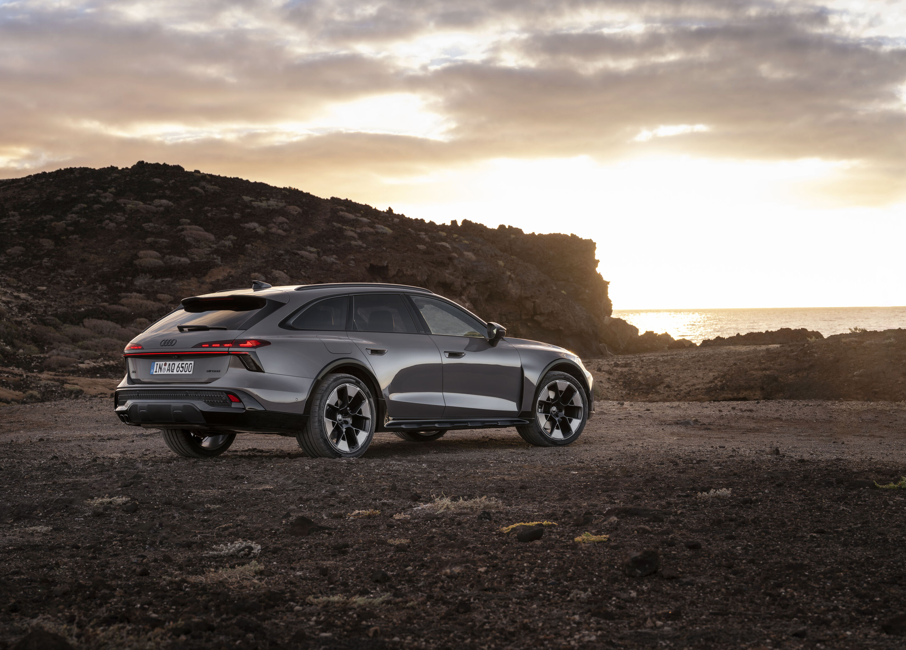 Audi A6 allroad quattro - Three-quarter rear view of the Audi A6 allroad (plateau grey metallic) against a coastal backdrop in backlight.