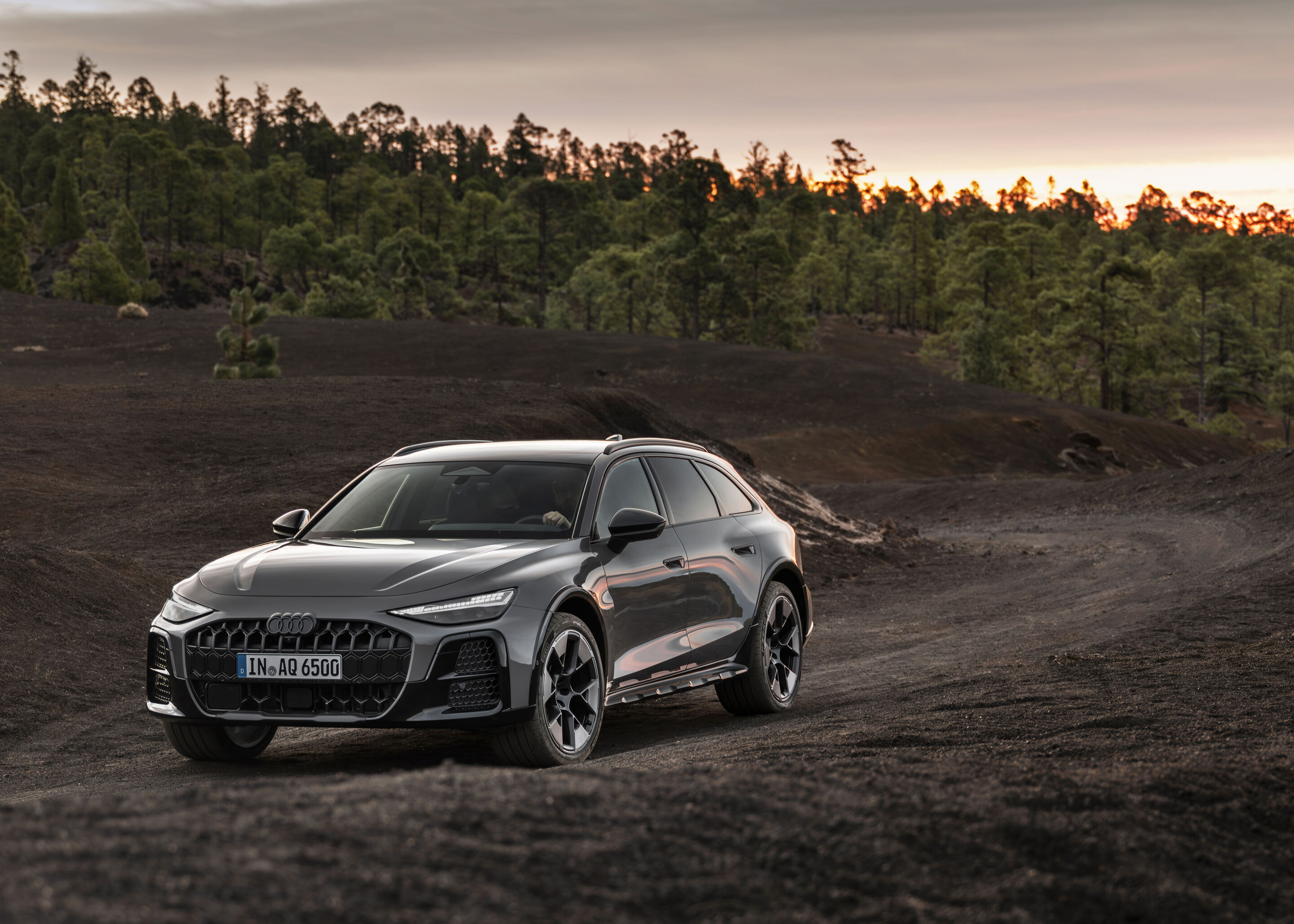 Audi A6 allroad quattro - i A6 allroad (plateau grey metallic) in a three-quarter front view on unpaved ground at dusk.