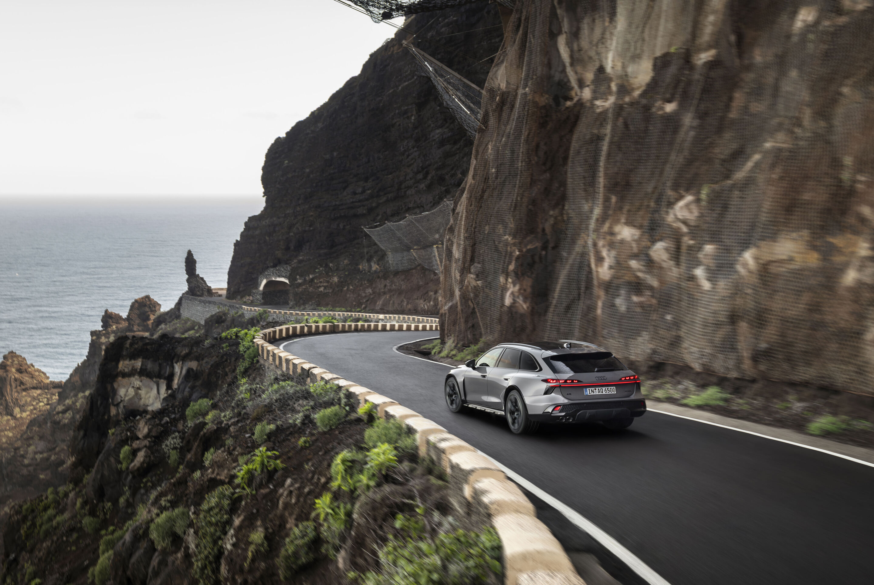 Audi A6 allroad quattro - Three-quarter rear view of Audi A6 allroad (plateau grey metallic) on a winding coastal road (dynamic shot).