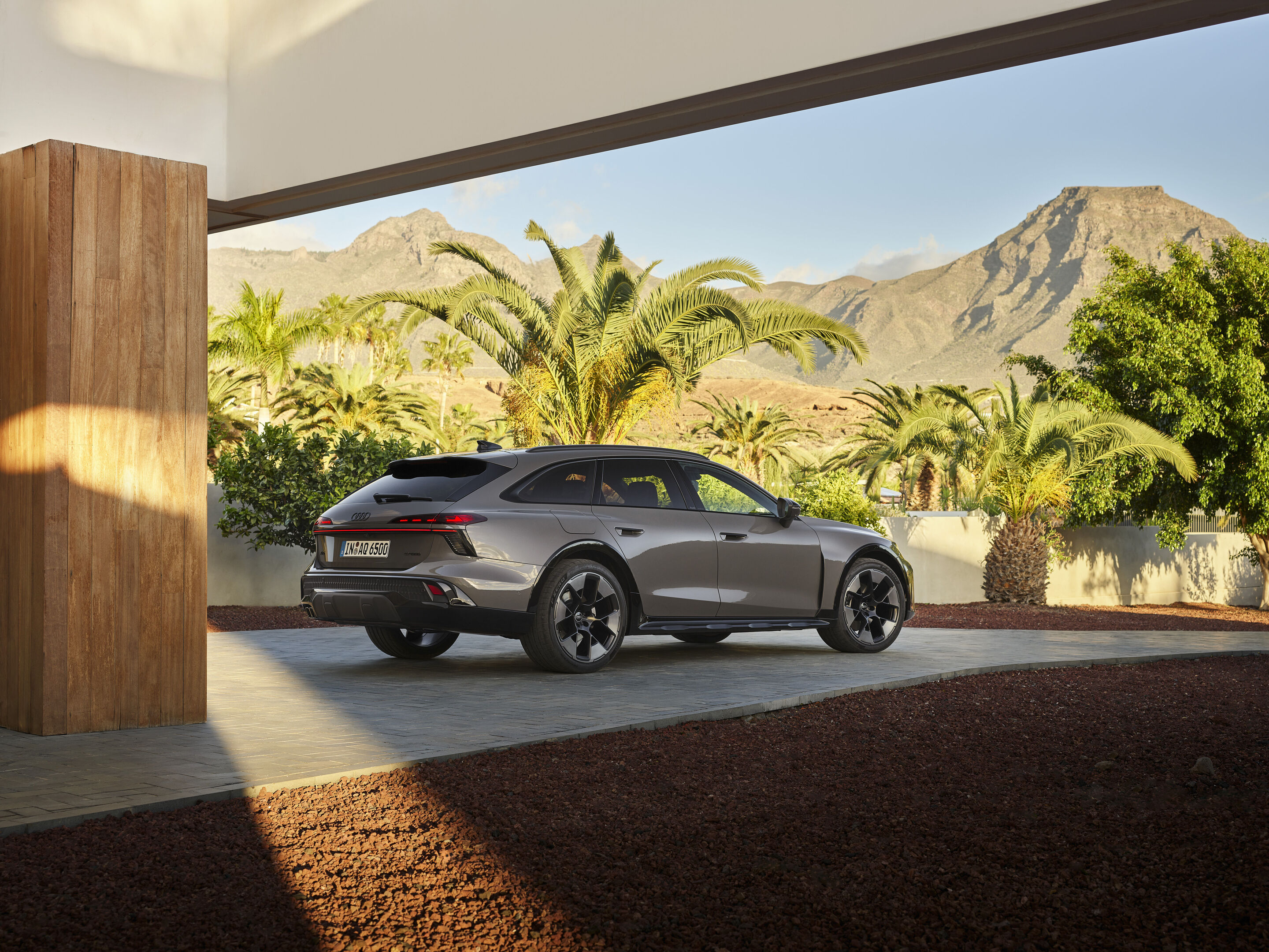 Audi A6 allroad quattro - Static three-quarter rear view of the Audi A6 allroad (plateau grey metallic) set in modern architecture with a striking mountain panorama in the background (static shot).