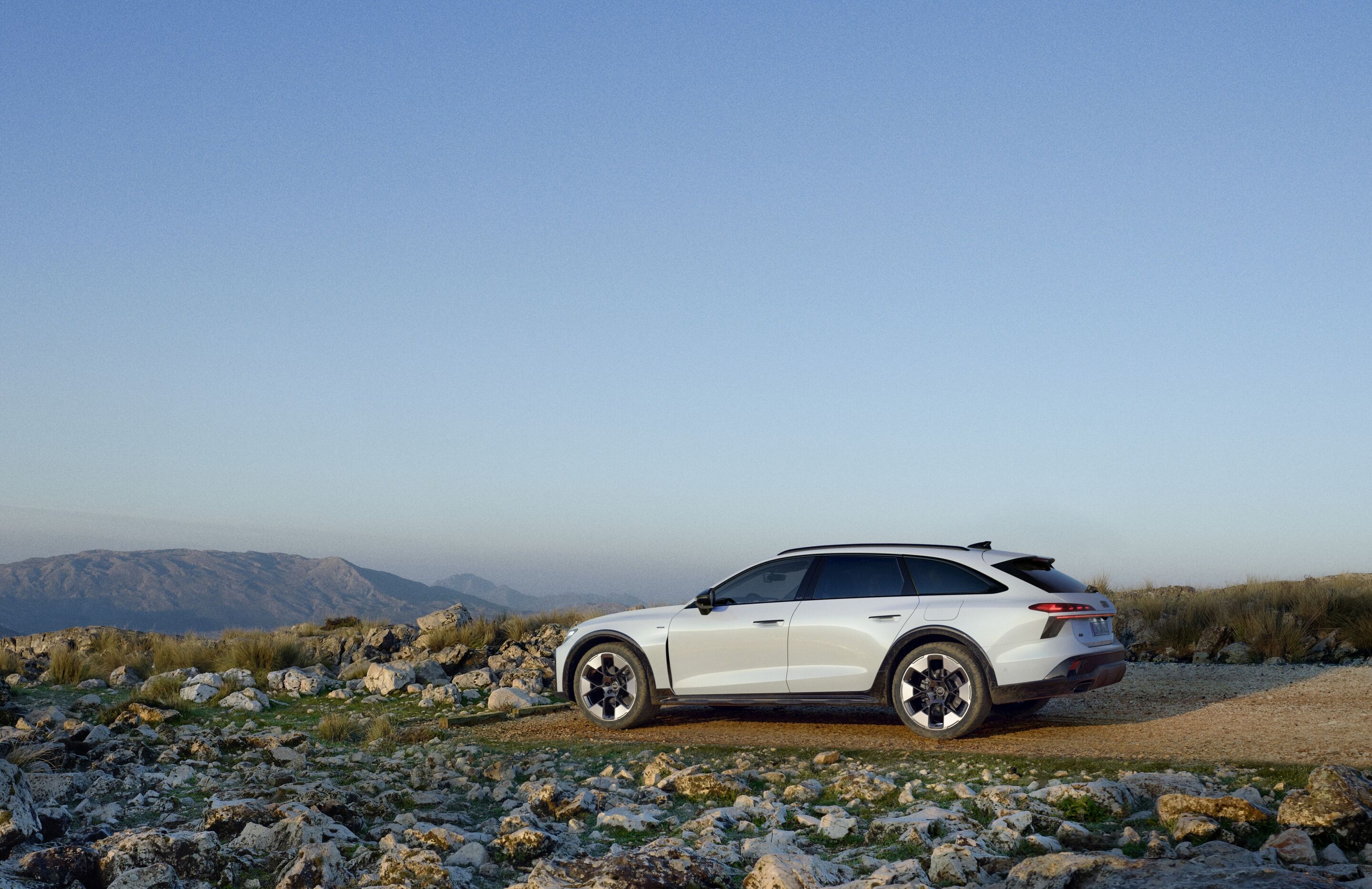 Audi A6 allroad e-hybrid quattro - Static shot: Audi A6 allroad e-hybrid (glacier white) on rocky terrain overlooking mountains.