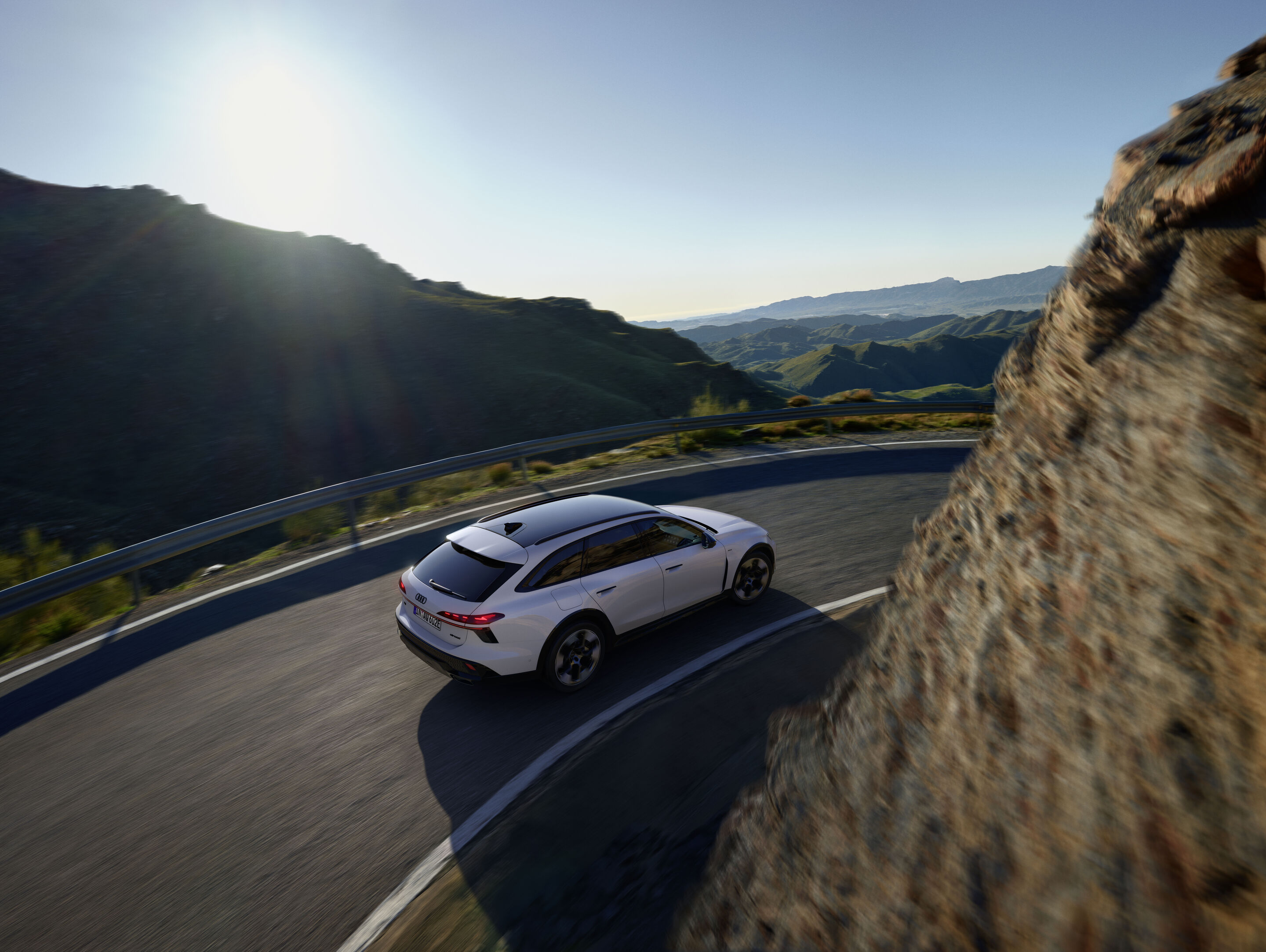 Audi A6 allroad e-hybrid quattro - Dynamic shot: Audi A6 allroad e-hybrid (glacier white) on a winding mountain road with expansive landscape views.