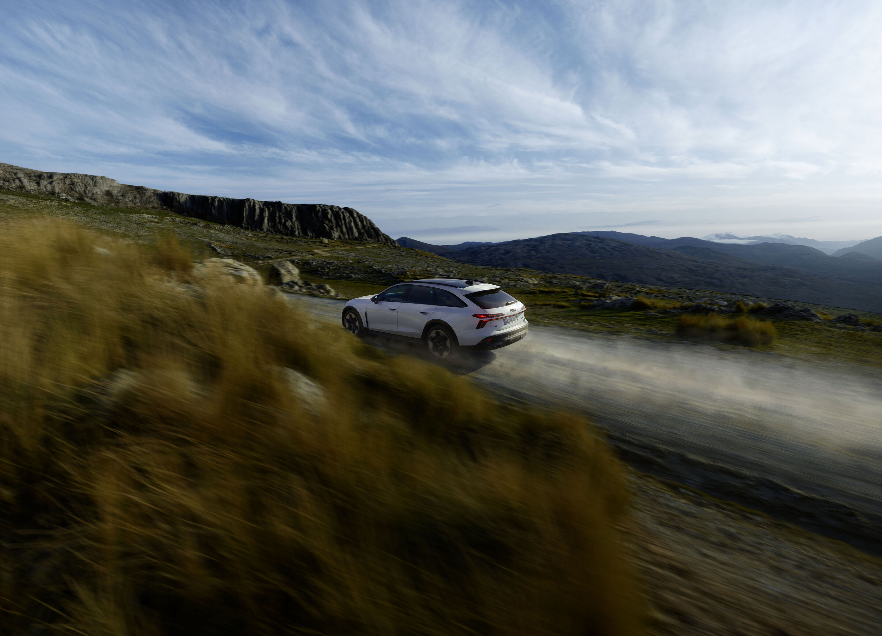 Audi A6 allroad e-hybrid quattro - Dynamic shot: Audi A6 allroad e-hybrid (glacier white) on a gravel road in a mountainous landscape – dynamic and controlled beyond paved roads.