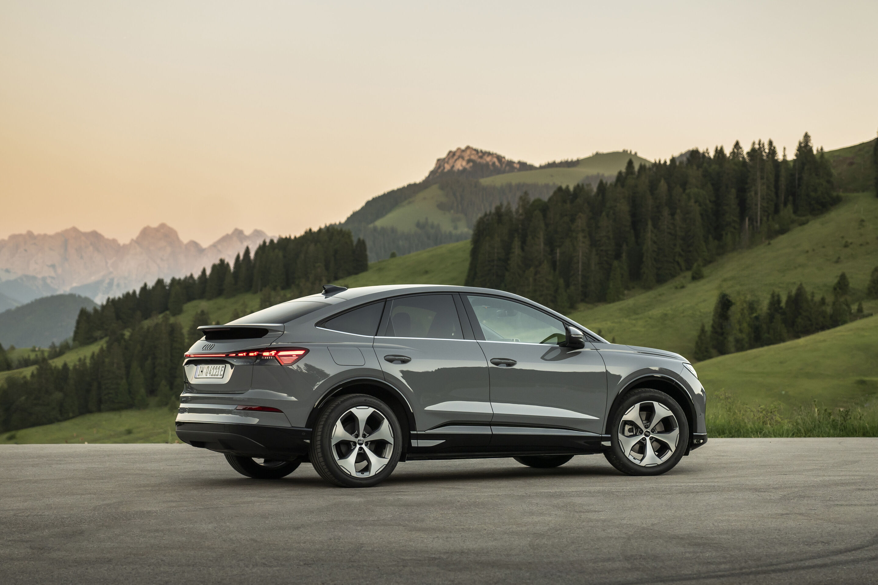 Ein Auto für jeden Moment: Unterwegs im Audi Q4 e-tron - Audi Q4 Sportback e-tron in Pebblegrau, Outdoor-Standaufnahme. Exterieur, Seitenansicht vor alpiner Bergkulisse.
