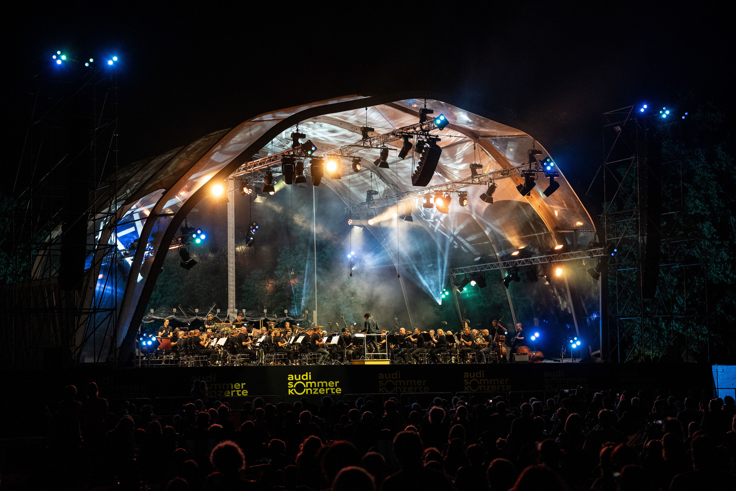 The Audi Wind Orchestra at the opening concert/classical open-air concert in Klenzepark - The Audi Wind Philharmonic, conducted by Mathias Wehr, performs beneath the illuminated stage structure in Klenzepark during the Classical Open-Air Concert of the...
