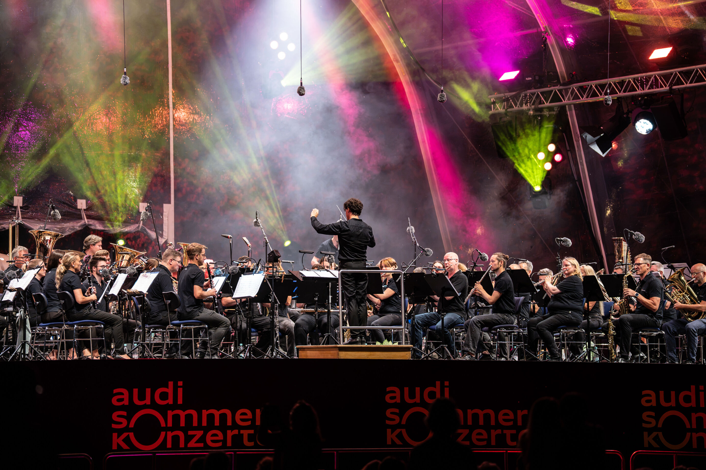 The Audi Wind Orchestra at the opening concert/classical open-air concert in Klenzepark - View from the audience towards the stage of the 2026 Classical Open-Air Concert in Klenzepark: The Audi Wind Philharmonic performs beneath the illuminated open-air...