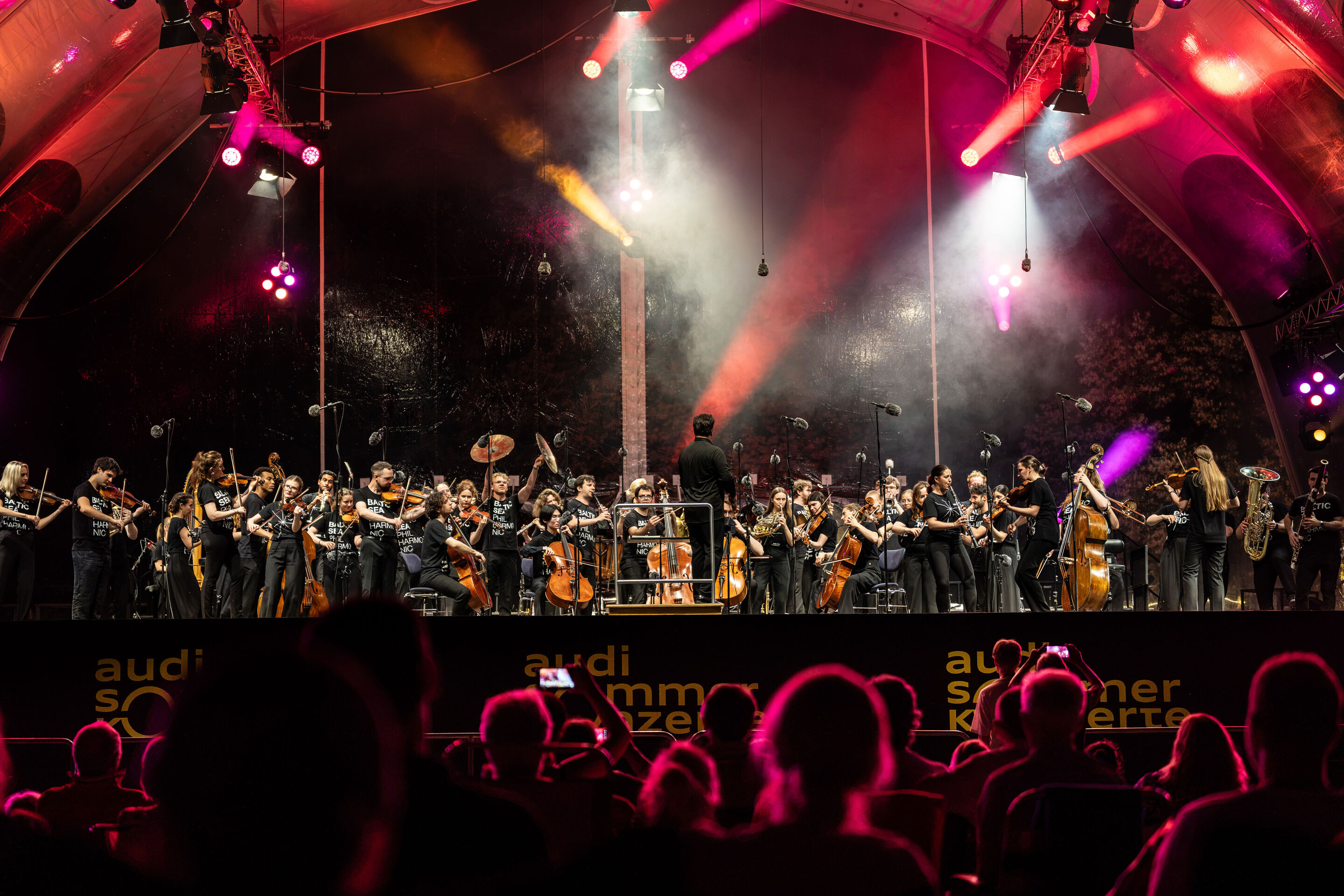 Baltic Sea Philharmonic performing at the classical open-air concert in Klenzepark - View from the audience towards the stage of the 2026 Classical Open-Air Concert in Klenzepark: The Baltic Sea Philharmonic performs beneath the illuminated open-air stage...